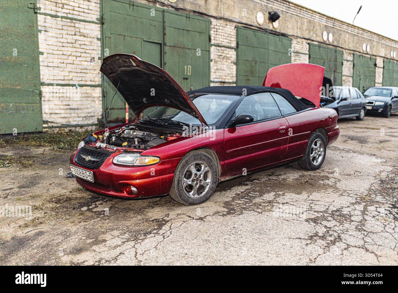Ein rotes Cabriolet mit offener Motorhaube in einem Garagenbereich mit mehreren Türen Stockfoto