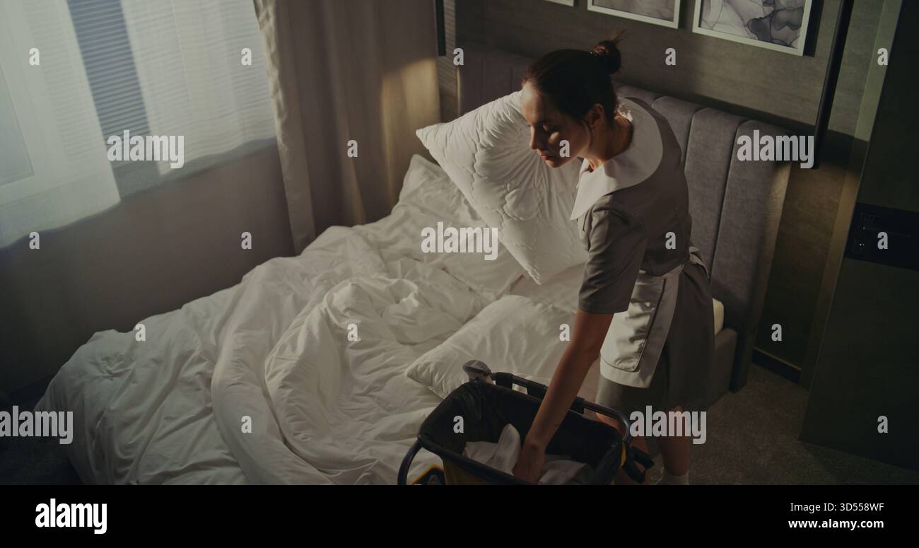 Hotelreinigung Personal Mit Trolley Ändert Bett Bettwäsche Gäste Abfahrt. Die Frau hebt und faltet die Handtücher vorsichtig und entfernt die Kissenbezüge von den Kissen. Konzept hohe Sauberkeitsstandards im Zimmer. Stockfoto