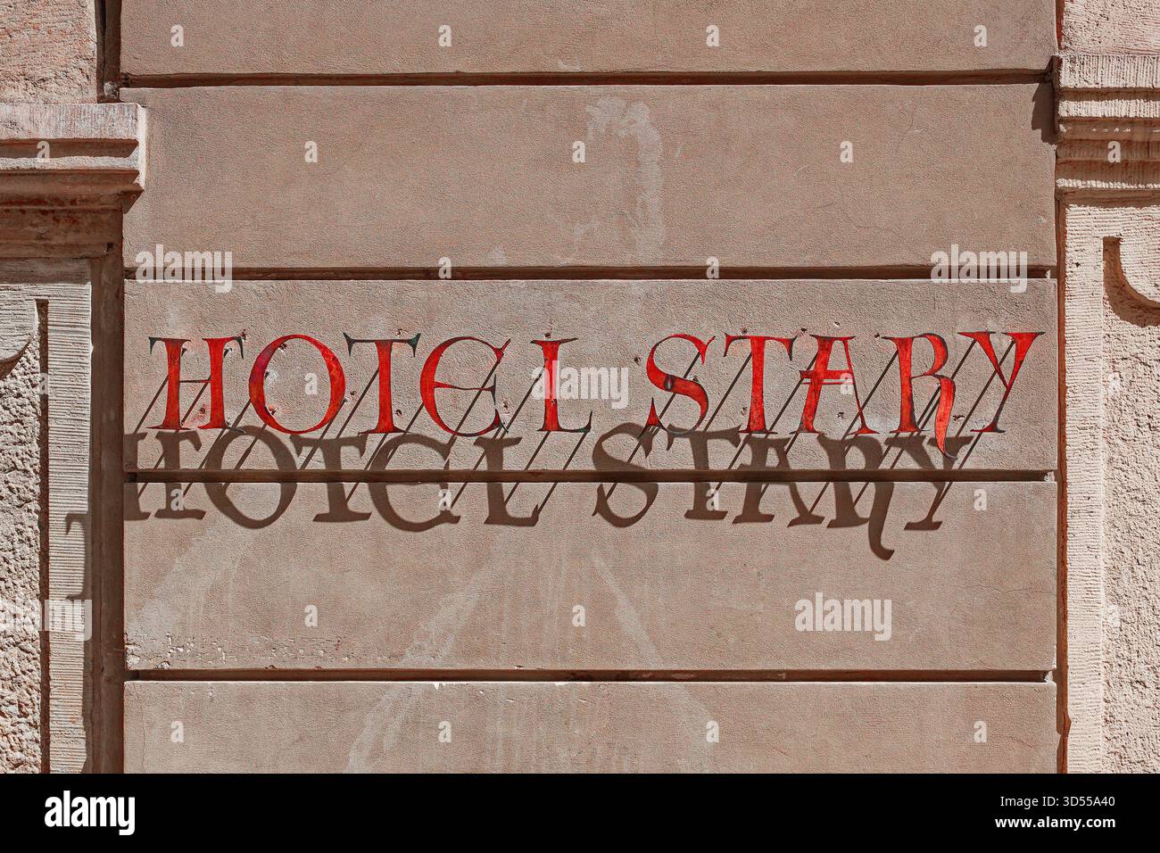 Sonnendurchfluteter Schriftzug „Hotel Stary“ wirft einen scharfen Schatten auf eine strukturierte Gebäudewand. Stockfoto
