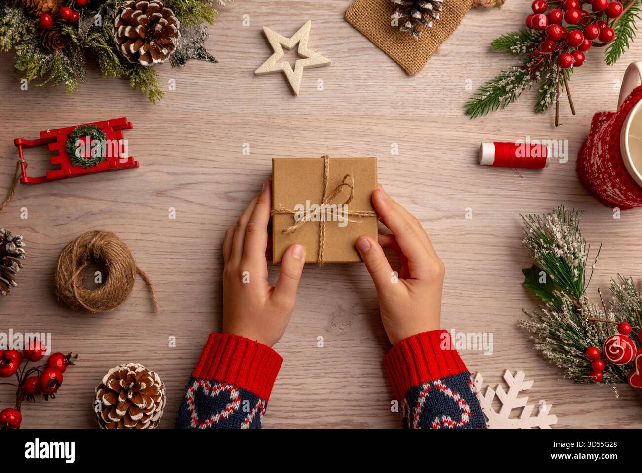 Kind mit einem umhüllten Weihnachtsgeschenk umgeben von festlicher Dekoration, das die Magie und Spannung der Kindheit während der Weihnachtszeit einfängt Stockfoto