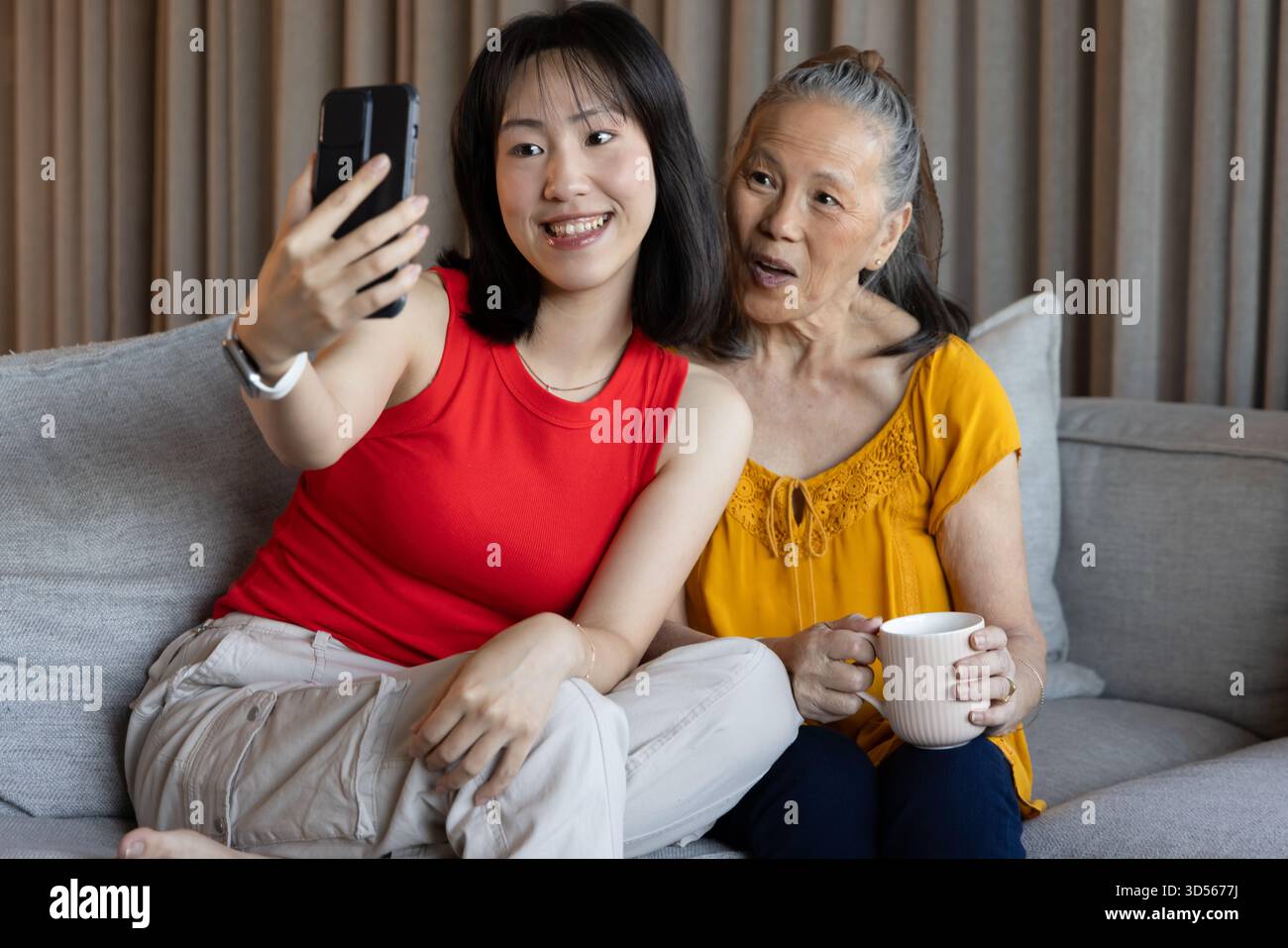 Selfie mit Großmutter machen, asiatische Frau lächelt auf der Couch und fängt den Moment ein Stockfoto