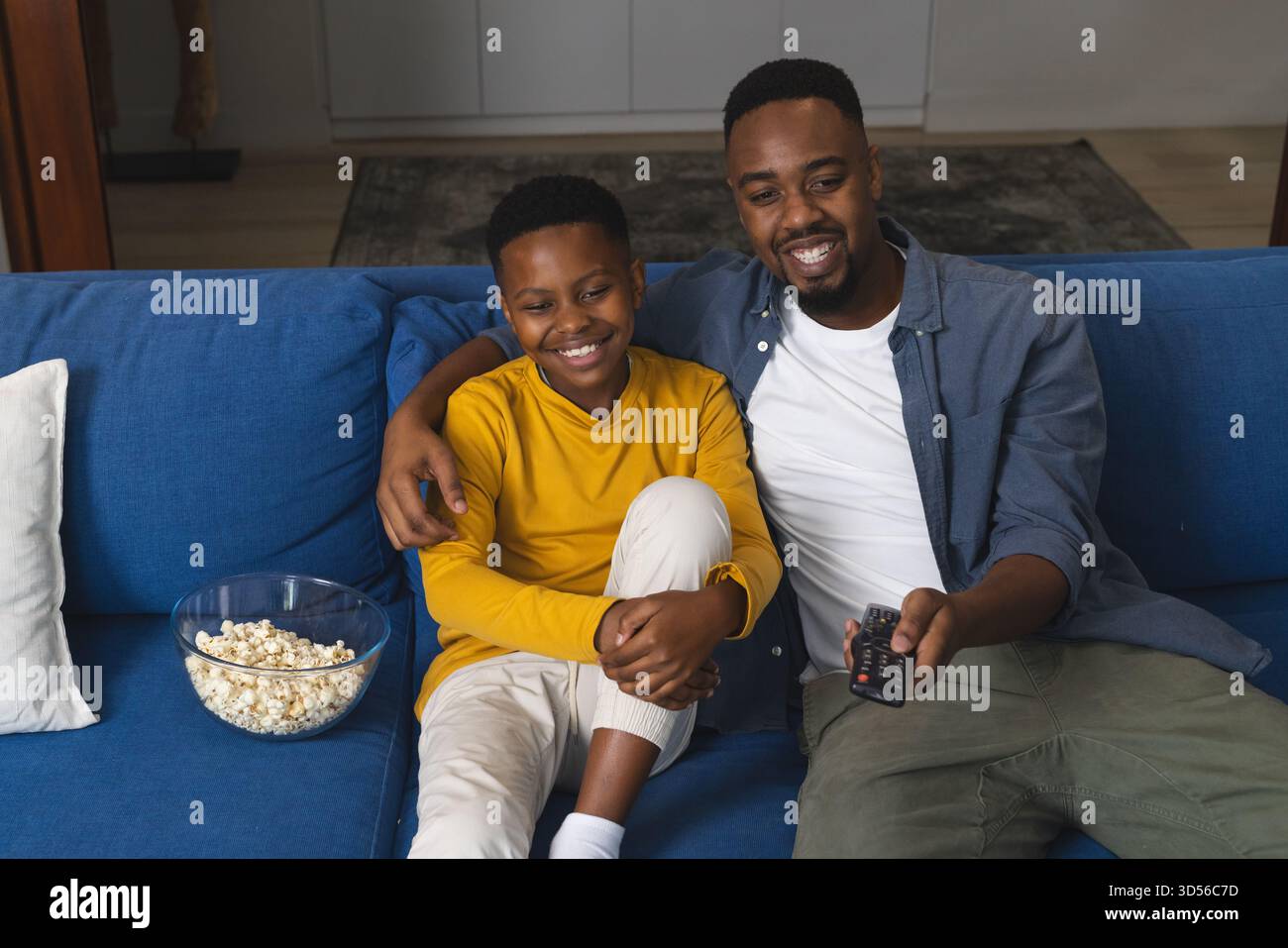 Vater und Sohn genießen Filmabend auf Couch mit Popcorn und Fernbedienung Stockfoto