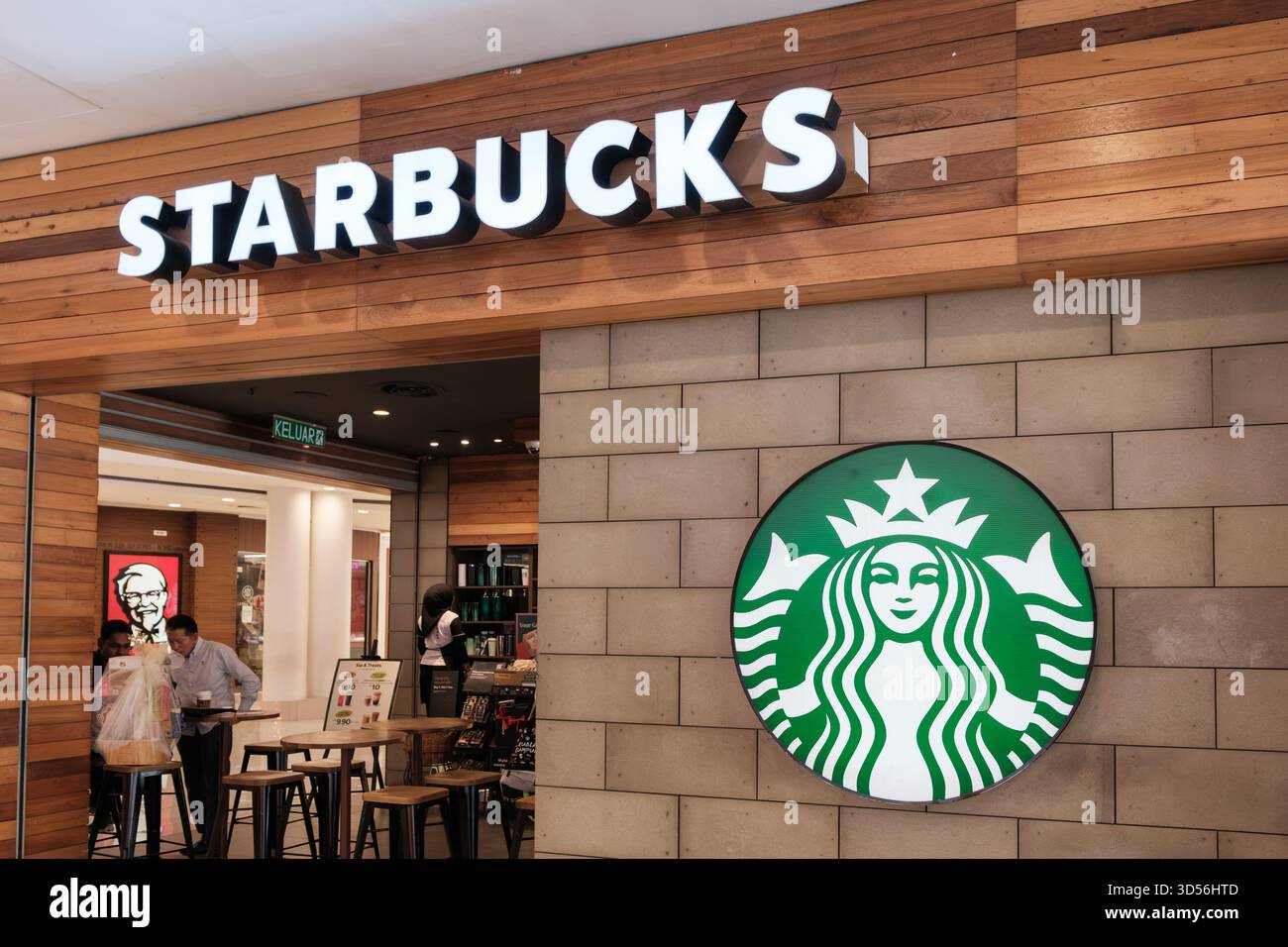 Das Café mit Starbucks-Marke verfügt über ein großes grünes Logo an der Steinwand mit Holzakzenten. Im Store werden Kaffeeprodukte ausgestellt, und das Ambiente ist hell Stockfoto