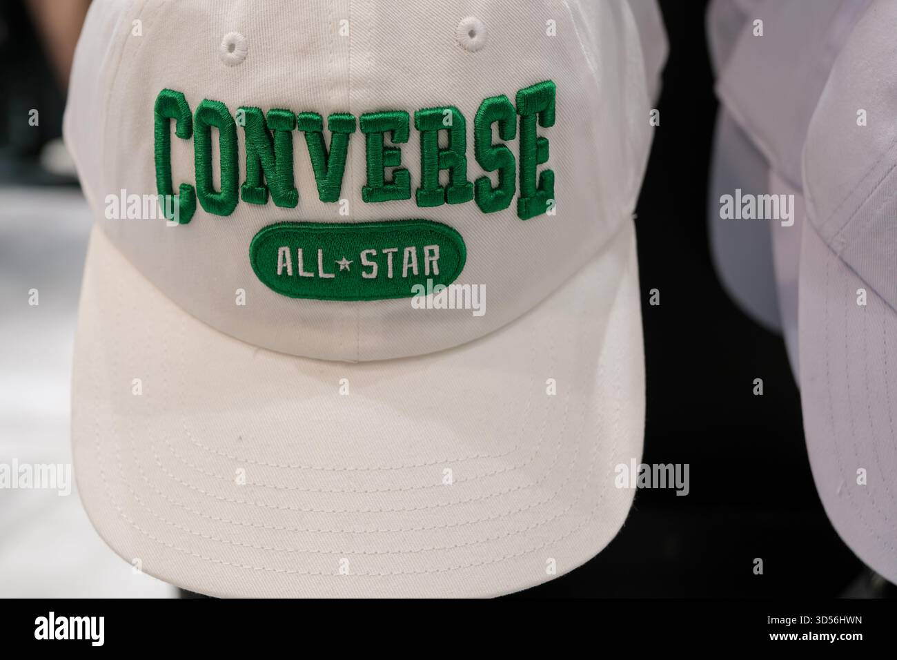 Penang, Malaysia – 16. Oktober 2025: Eine weiße Converse All Star-Kappe mit grüner Stickerei ist auf einem Regal sichtbar und zeigt ihr Logo Stockfoto