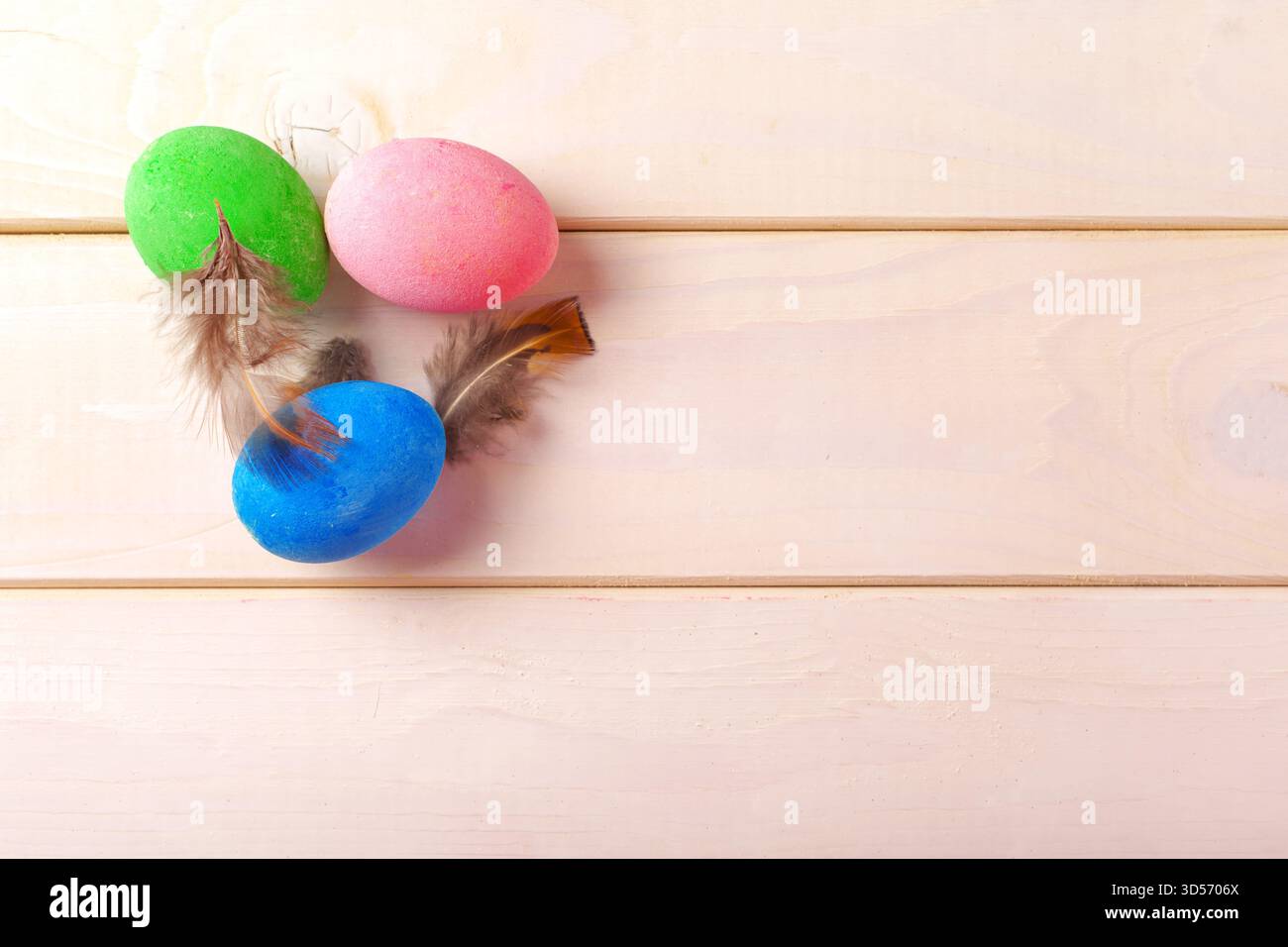 Farbenfrohe Ostereier mit Federn auf hellem Holzhintergrund für Frühlingsfeste Stockfoto