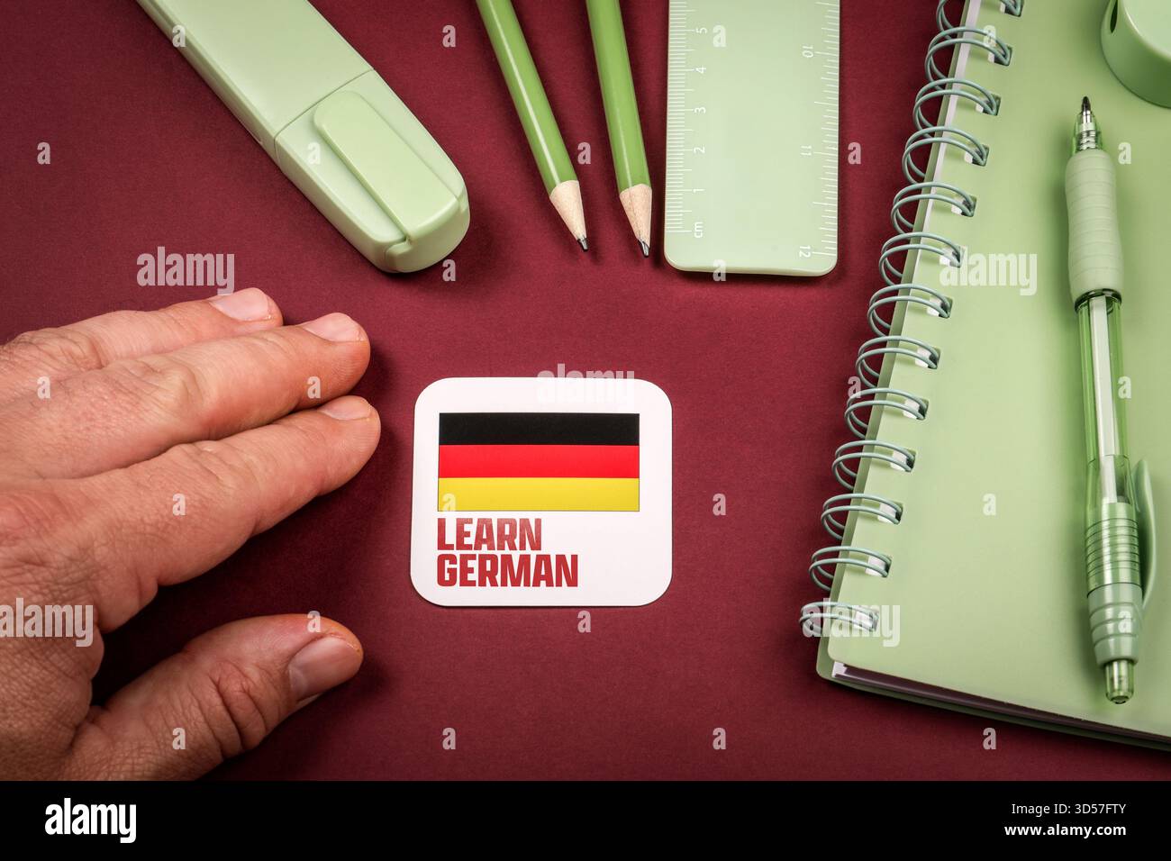 Hand neben, um Deutsch zu lernen Karte mit Deutschland Flagge umgeben von Briefpapier und Notizbuch, Konzept des Studiums Fremdsprache und Bildung. Stockfoto