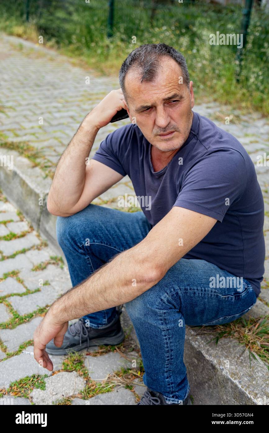 Mann, der auf einem Bordstein sitzt und in die Ferne blickt Stockfoto