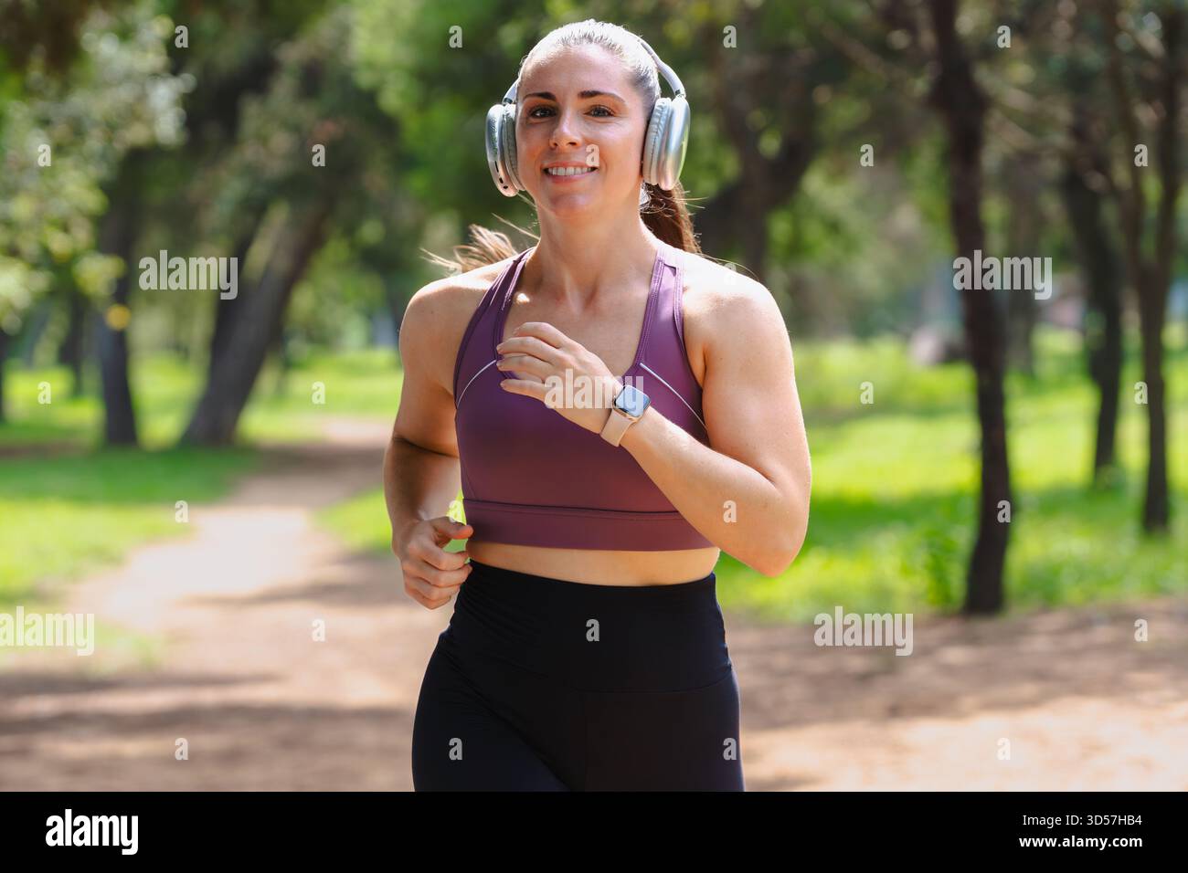 Junge Frau, die draußen auf dem Parkweg joggt, mit Sportbekleidung und Kopfhörern Stockfoto