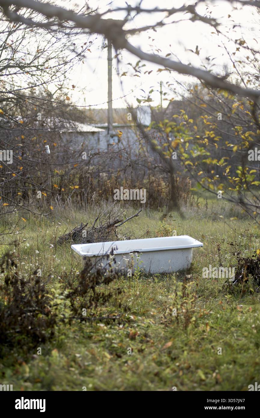 Verlassene weiße Badewanne, die auf dem bewachsenen Landhof sitzt Stockfoto