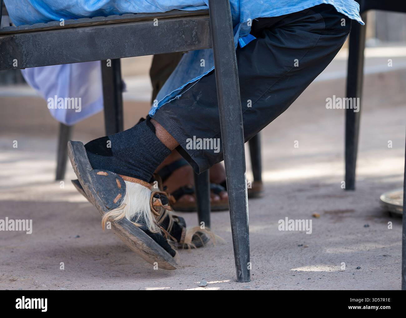 Traditionelle marokkanische Sandalen mit Haarklemmen, die unter einem Tisch im Freien getragen werden. Nahaufnahme handgefertigter Ledersandalen. Stockfoto