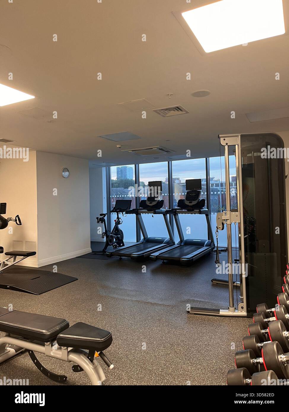 Eine saubere und moderne Inneneinrichtung des Fitnessstudios in Leeds, England, mit Laufbändern, Gewichten und großen Fenstern mit Blick auf die Stadt. Helle Beleuchtung und minimalistisch Stockfoto