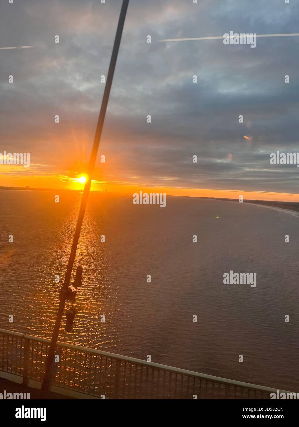 Ein atemberaubender Sonnenaufgang über dem Wasser in Hull, England, mit der goldenen Sonne, die eine helle Reflexion über die ruhige Oberfläche wirft. Weiche Morgenwolken kleben - Smartphone-aufgenommenes Stockfoto