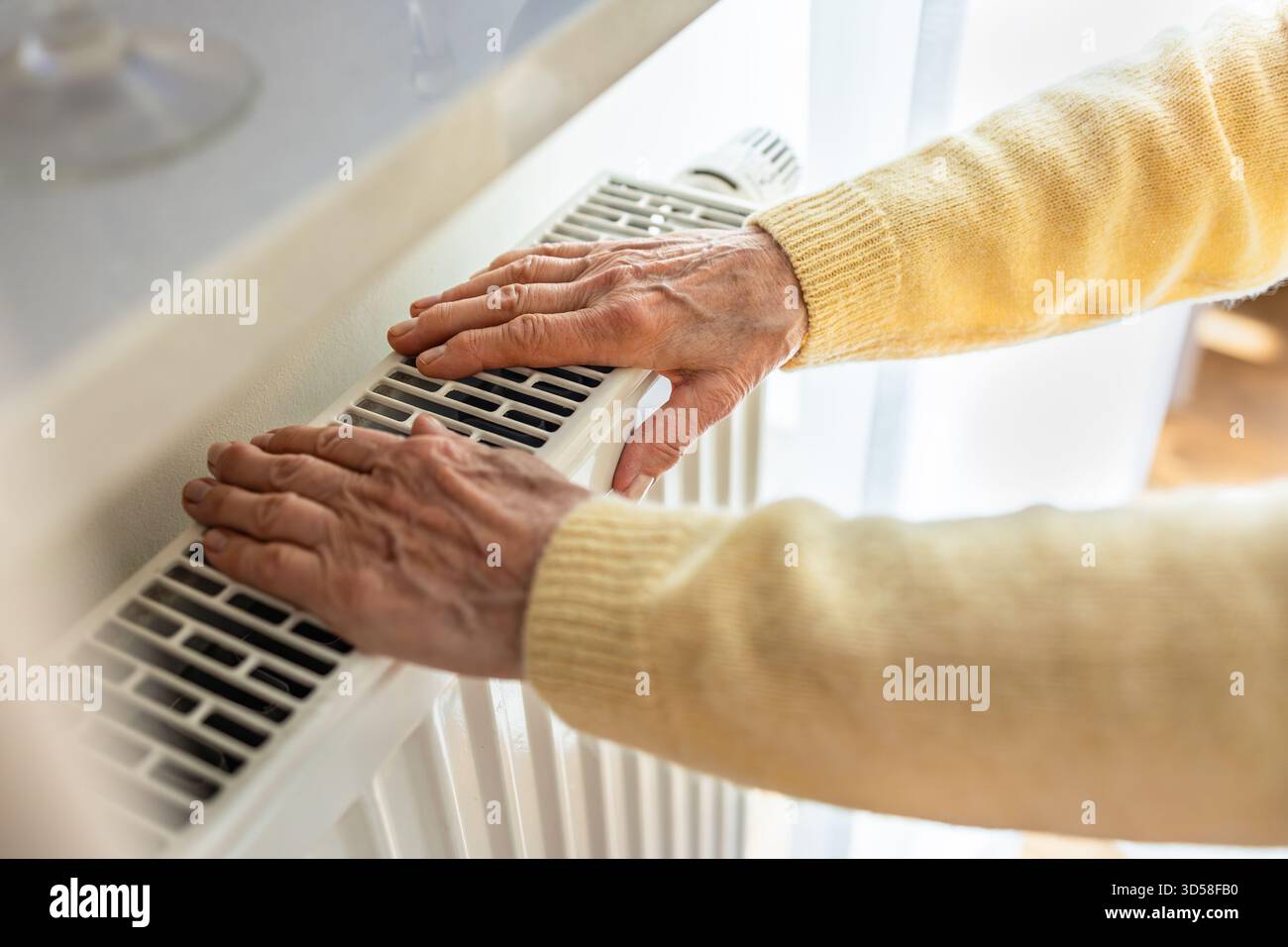 Eine ältere Frau wärmt ihre Hände auf einem Heizkörper zu Hause, Nahaufnahme Stockfoto