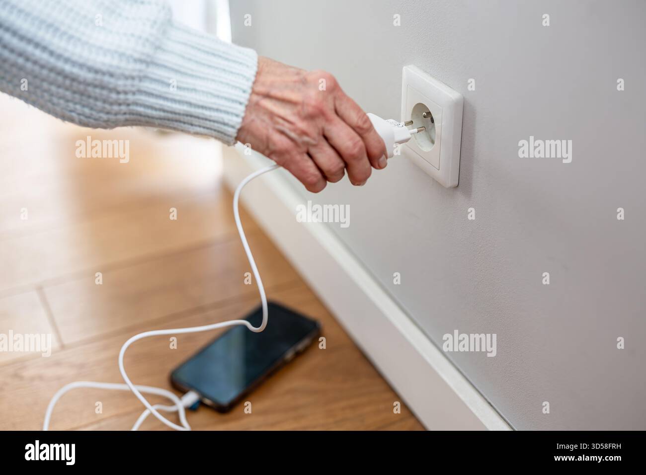 Nahaufnahme einer älteren Frau, die einen Netzstecker in eine Steckdose steckte, um ihr Telefon aufzuladen Stockfoto