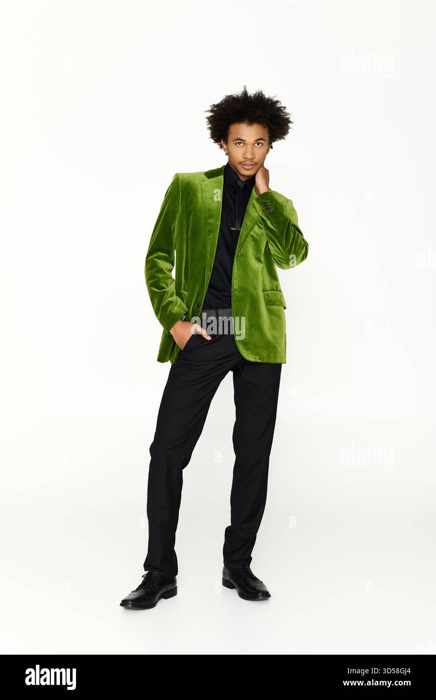 Ein hübscher junger Mann in einem grünen Blazer posiert selbstbewusst vor einem einfachen Hintergrund. Stockfoto