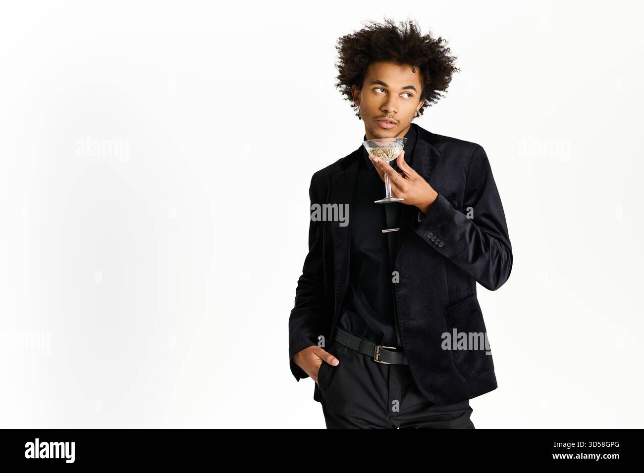 Ein hübscher junger Mann schlürft einen Cocktail und zeigt Eleganz mit seiner raffinierten Kleidung. Stockfoto