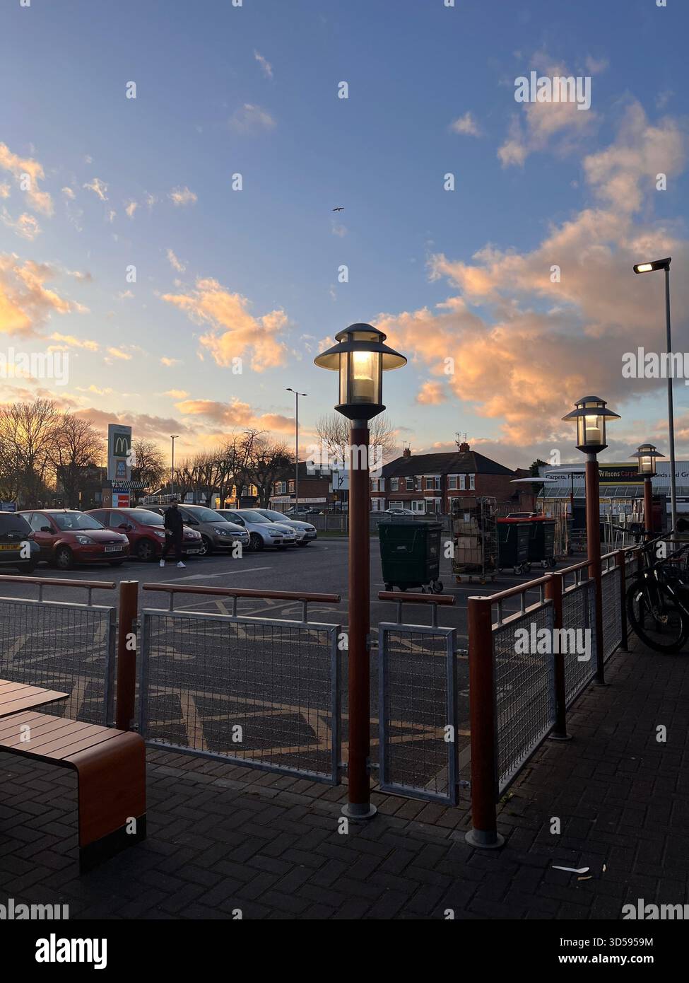 Ein warmer Sonnenuntergang beleuchtet eine ruhige Straße in Hull, England, mit klassischen Laternenpfosten und sanften Abendfarben. Die friedliche Stadtszene fängt das Ende ein. - Smartphone-aufgenommenes Stockfoto