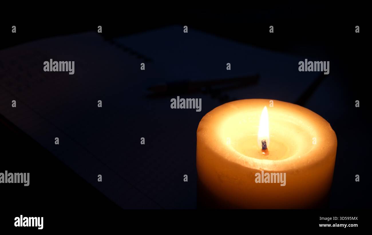 Eine warme Kerze leuchtet bei schwachem Licht sanft neben einem Notebook und lädt zu Gedanken und Frieden ein. Stockfoto