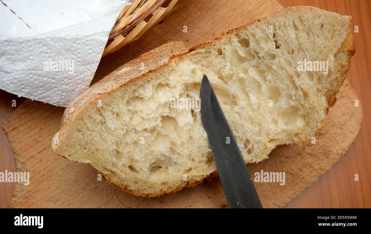 Warmes Brot liegt auf einem hölzernen Schneidebrett, während ein Messer seine weiche Mitte durchschneidet. Stockfoto