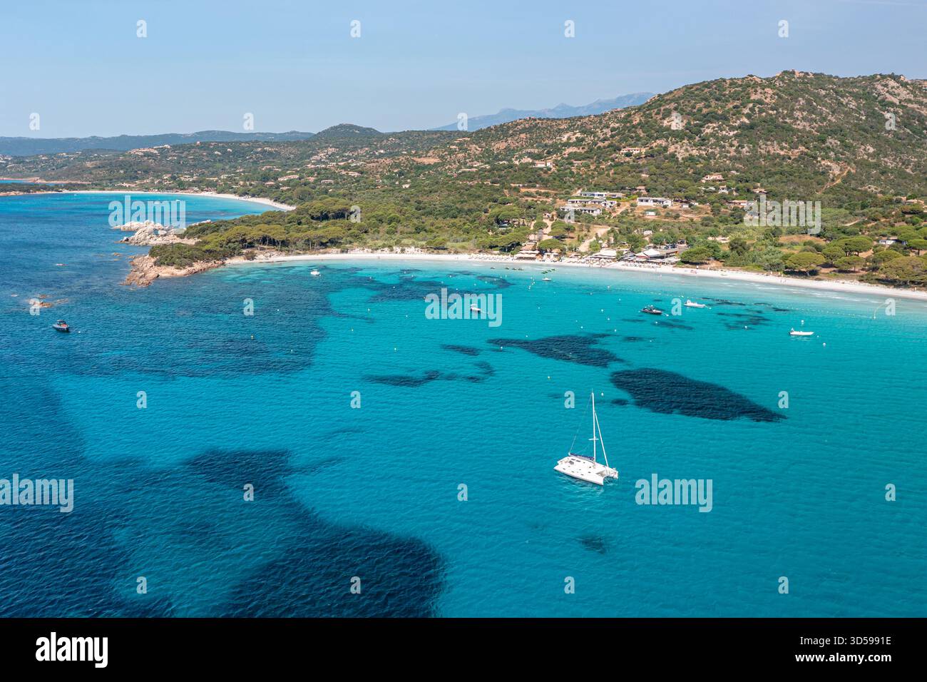 Helles türkisfarbenes Wasser trifft auf einen weißen Sandstrand, mit einer einsamen Segelyacht vor der Küste, Korsika, Frankreich Stockfoto