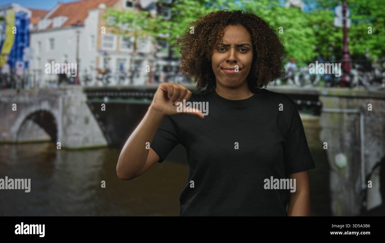 Frau zeigt auf einer amsterdamer Straße an einer Kanalbrücke mit Fahrrädern und Bäumen die Daumen nach unten; Kritik an der Missbilligung. Stockfoto