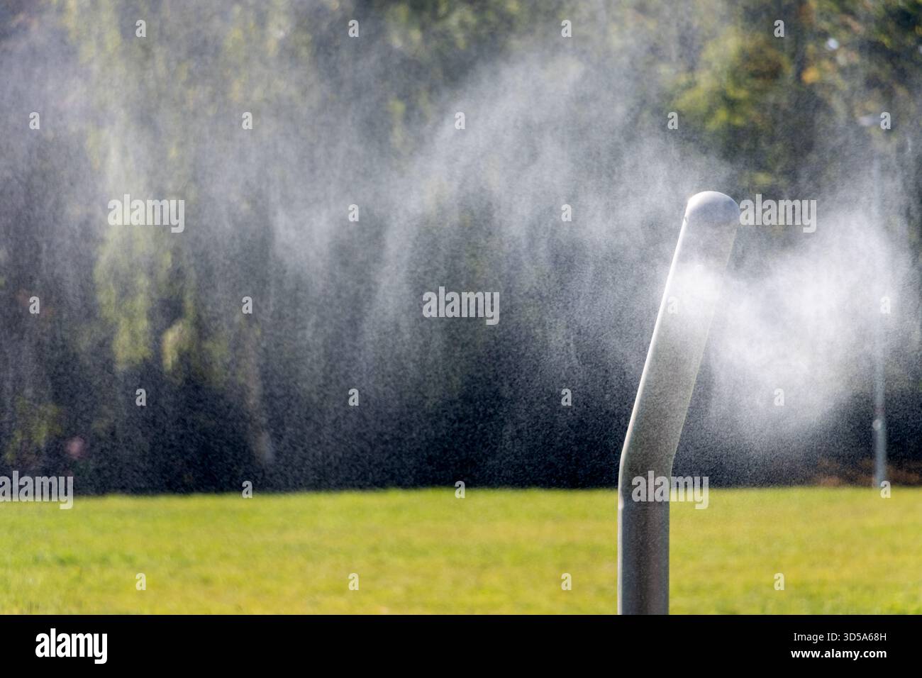 Wasserregner sprüht an sonnigen Tagen einen feinen Nebel über den Rasen in einem grünen Park Stockfoto