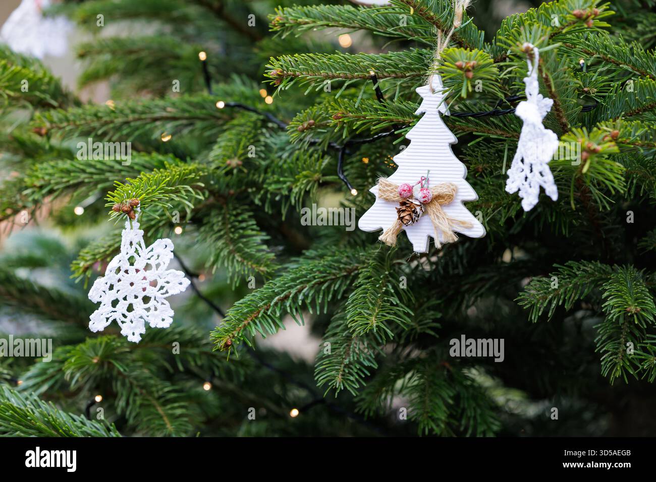 Gemütlicher Weihnachtsbaum mit handgefertigtem Kunsthandwerk. Weihnachtsbaumzweig mit handgefertigten weißen Ornamenten. Stockfoto