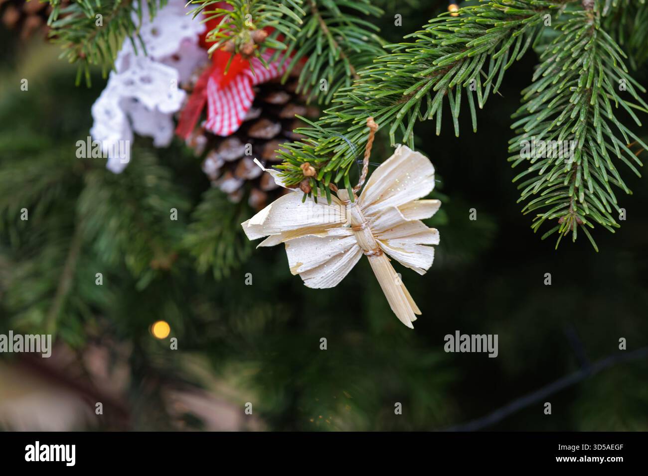 Strohengel handgefertigtes Weihnachtsschmuck auf grünem Tannenzweig. Rustikale festliche Einrichtung. Stockfoto