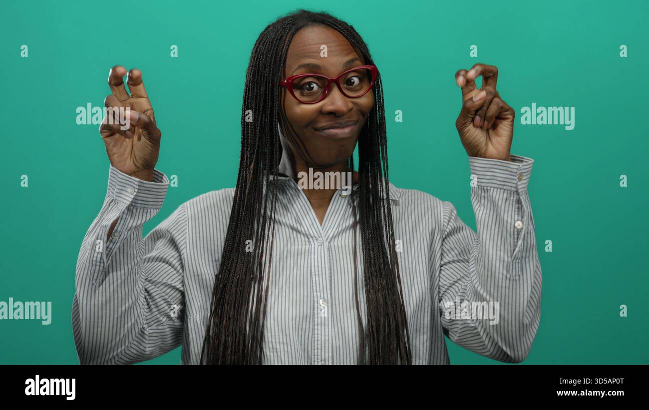Frau mit langen Haaren und einer Brille, die Zitate vor grünem Hintergrund macht, gestreiftes Hemd trägt, Selbstvertrauen und Humor ausstrahlt. Stockfoto