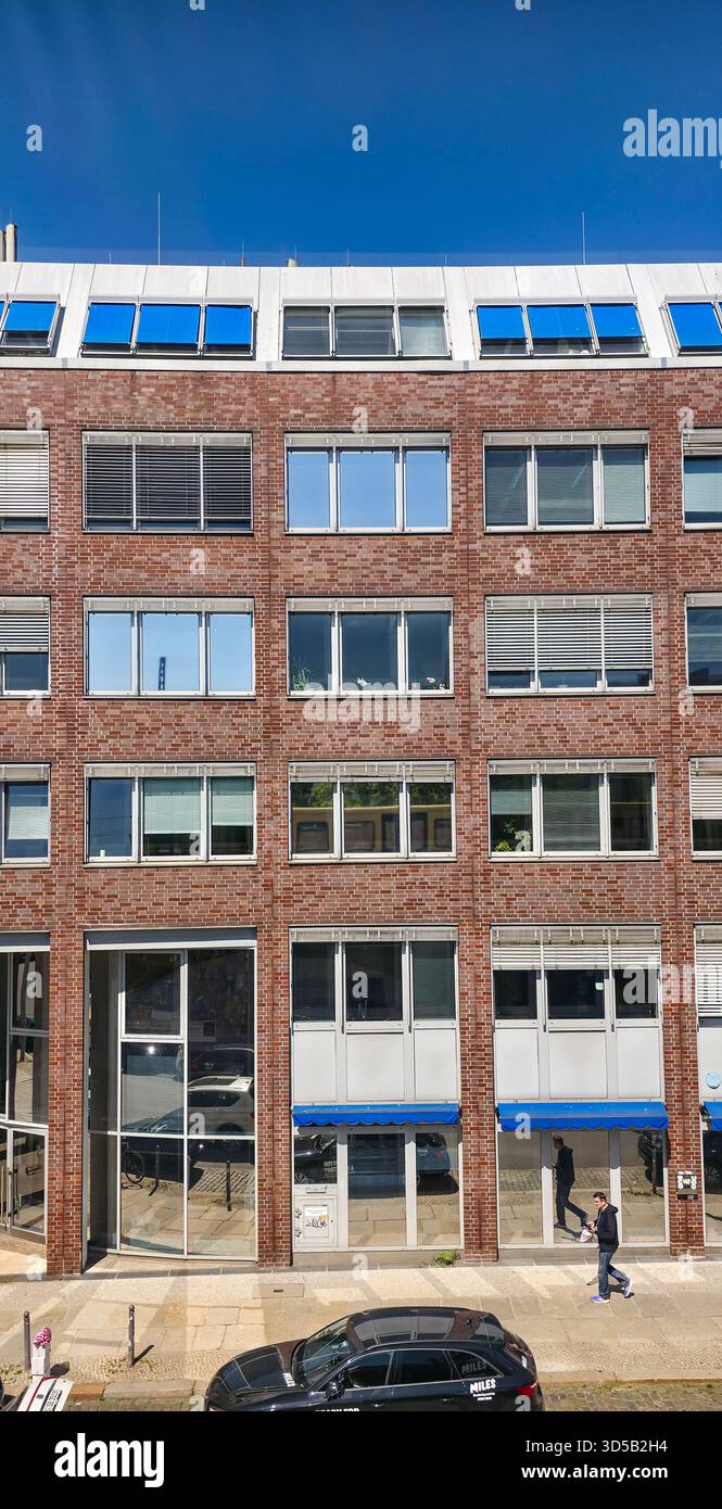 Berlin, Deutschland - 13. Mai 2025: Moderne Backsteinbürostruktur mit großen Fenstern und blauen Markisen zeigt städtische Architektur und Design. - Smartphone-aufgenommenes Stockfoto