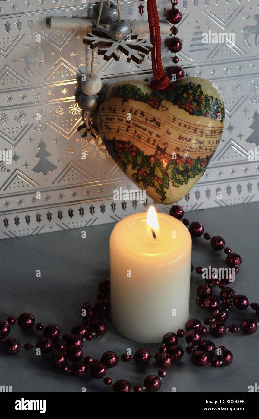 Weiße brennende Weihnachtskerze mit herzförmiger Weihnachtsdekoration, Noten-Ornament, Weihnachtsgrußkarte Stockfoto