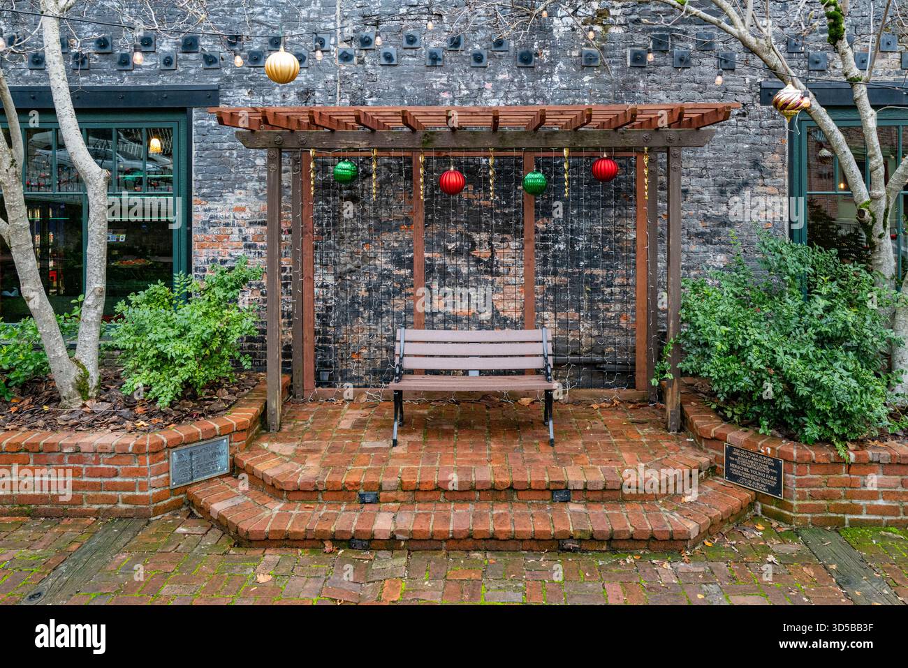 Eine gemütliche Bank im Herschel Young Park in der Altstadt von Auburn, umgeben von historischen Backsteinen und Weihnachtsdekorationen. Stockfoto