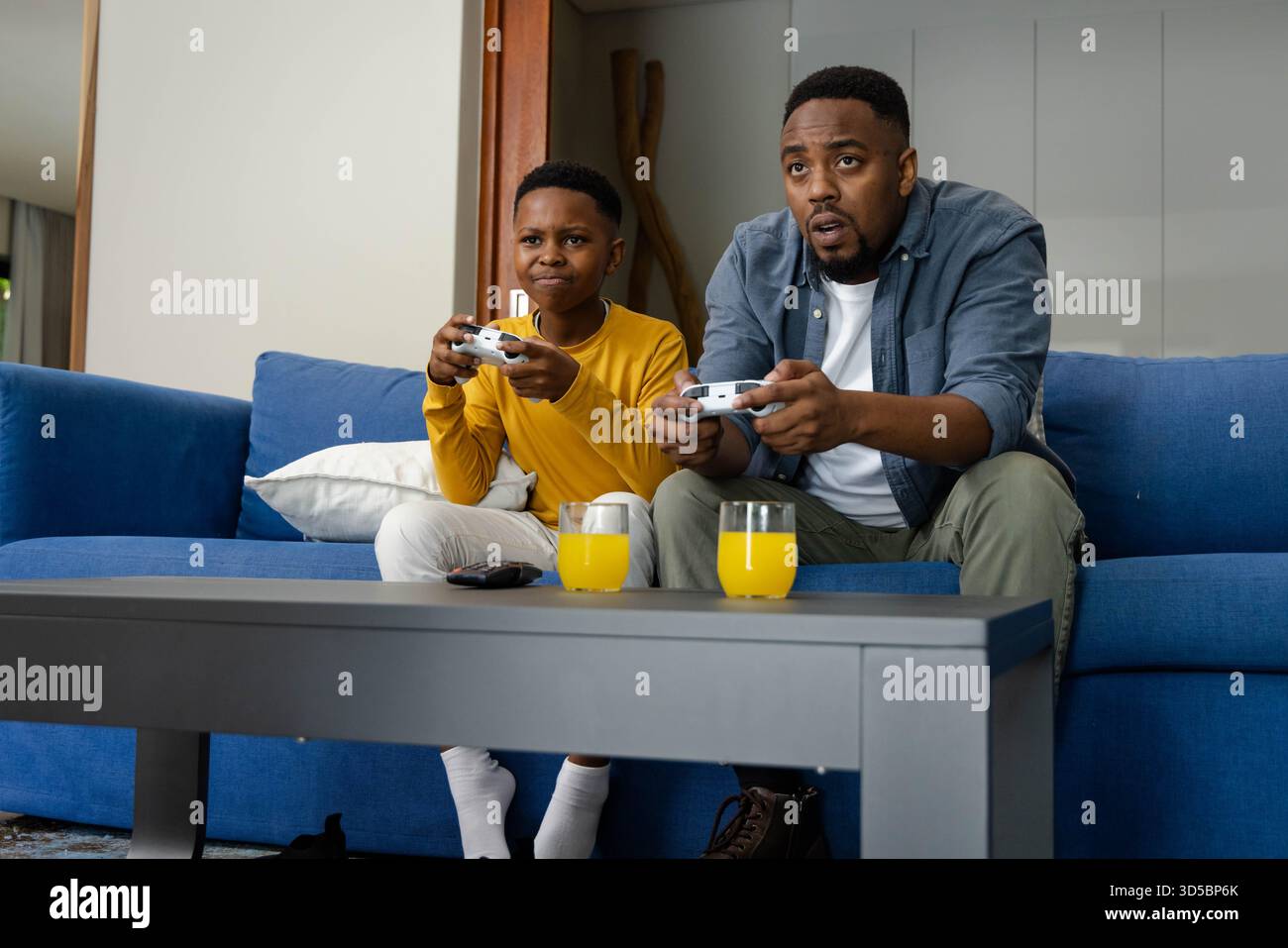 Afroamerikanischer Vater und Sohn spielen Videospiele auf der Couch und genießen eine gute gemeinsame Zeit Stockfoto
