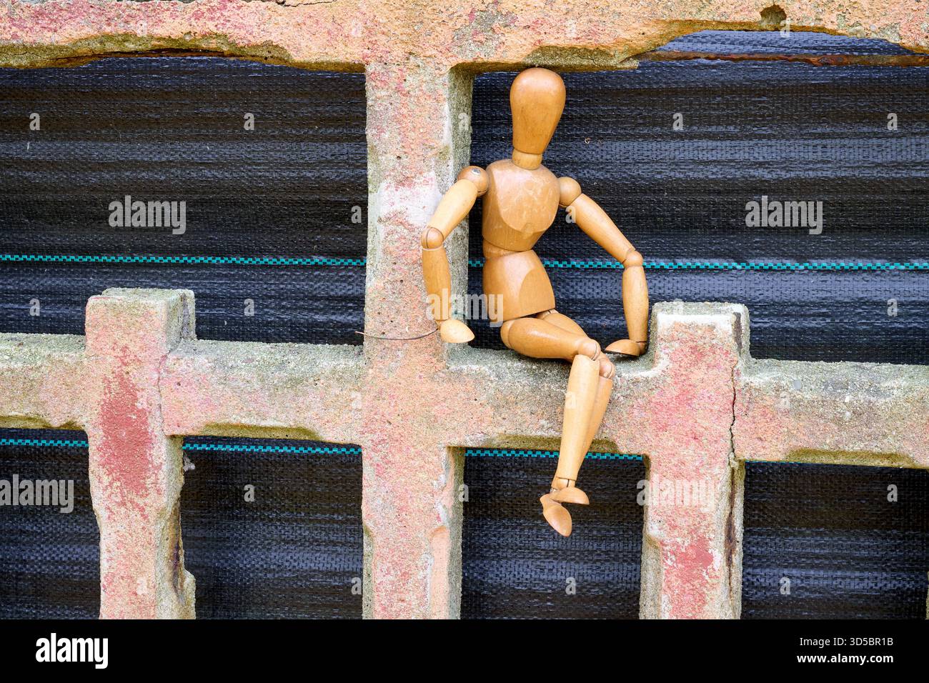 Unsere Tür, hölzerne Puppe, die an der Gartenwand sitzt Stockfoto