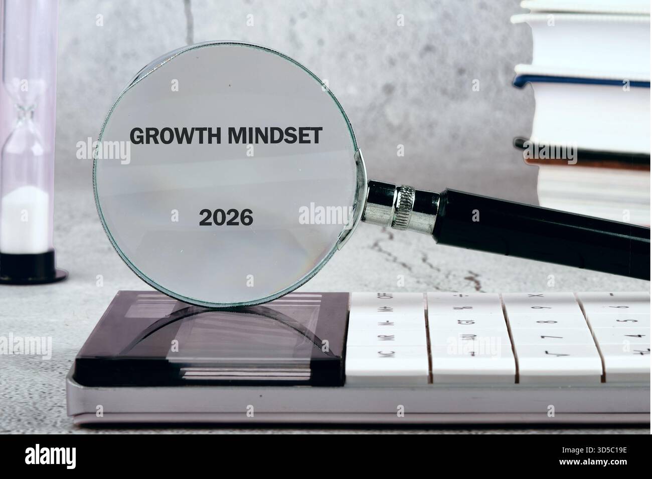 Eine Lupe zeigt die Wörter Growth Mindset und das Jahr 2026. Eine Sanduhr, ein Taschenrechner und ein Stapel Bücher sitzen in der Nähe auf einer steinähnlichen Oberfläche. Stockfoto