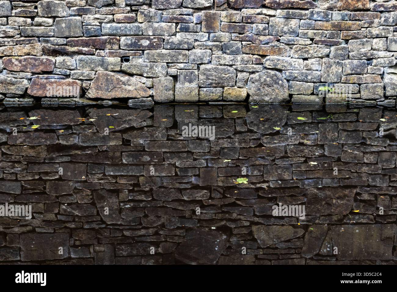 Die Steinkanalwand spiegelt sich in stillem Wasser Stockfoto