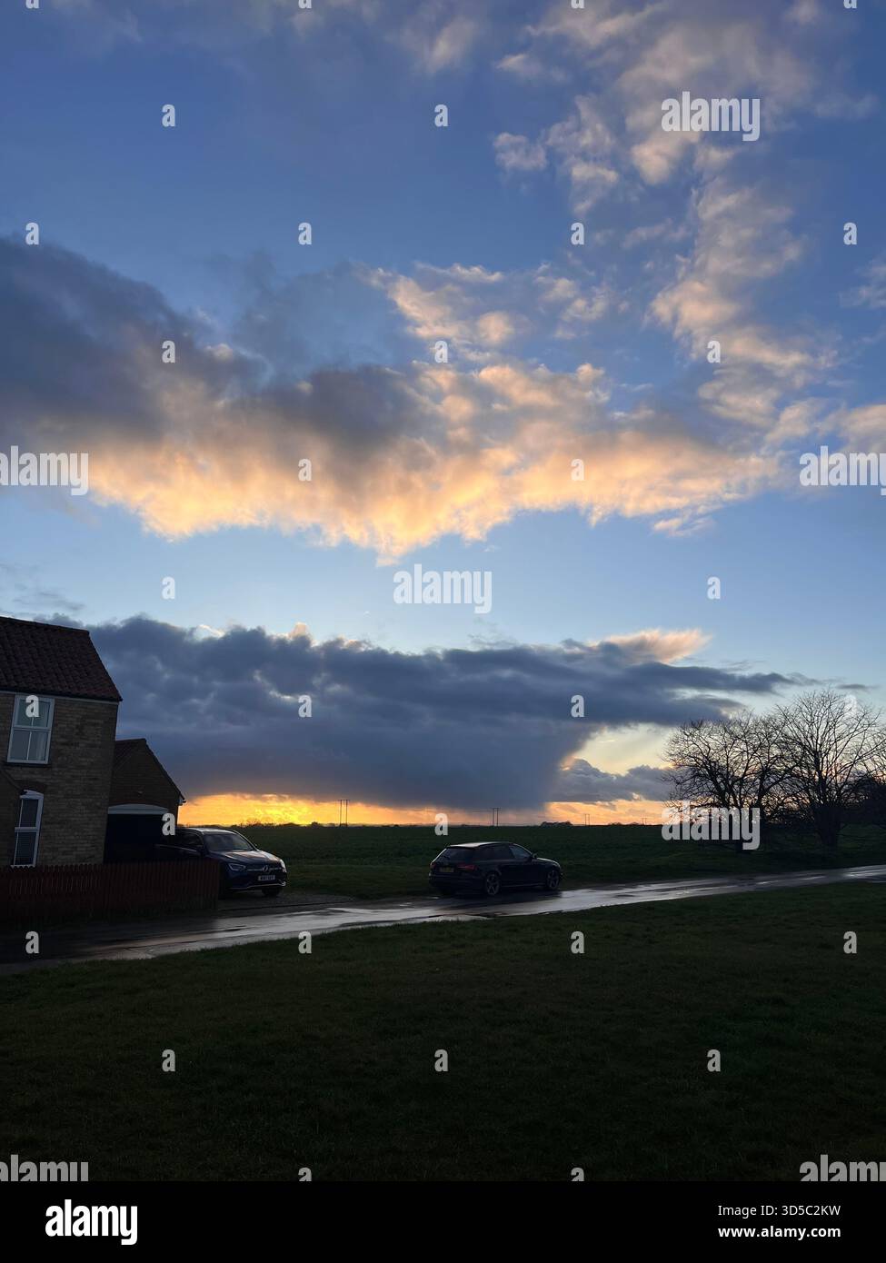 Dunkle Sturmwolken, die sich über eine ruhige Vorstadtstraße mit geparkten Autos während des goldenen Sonnenuntergangs in Hull, England, wälzen. - Smartphone-aufgenommenes Stockfoto