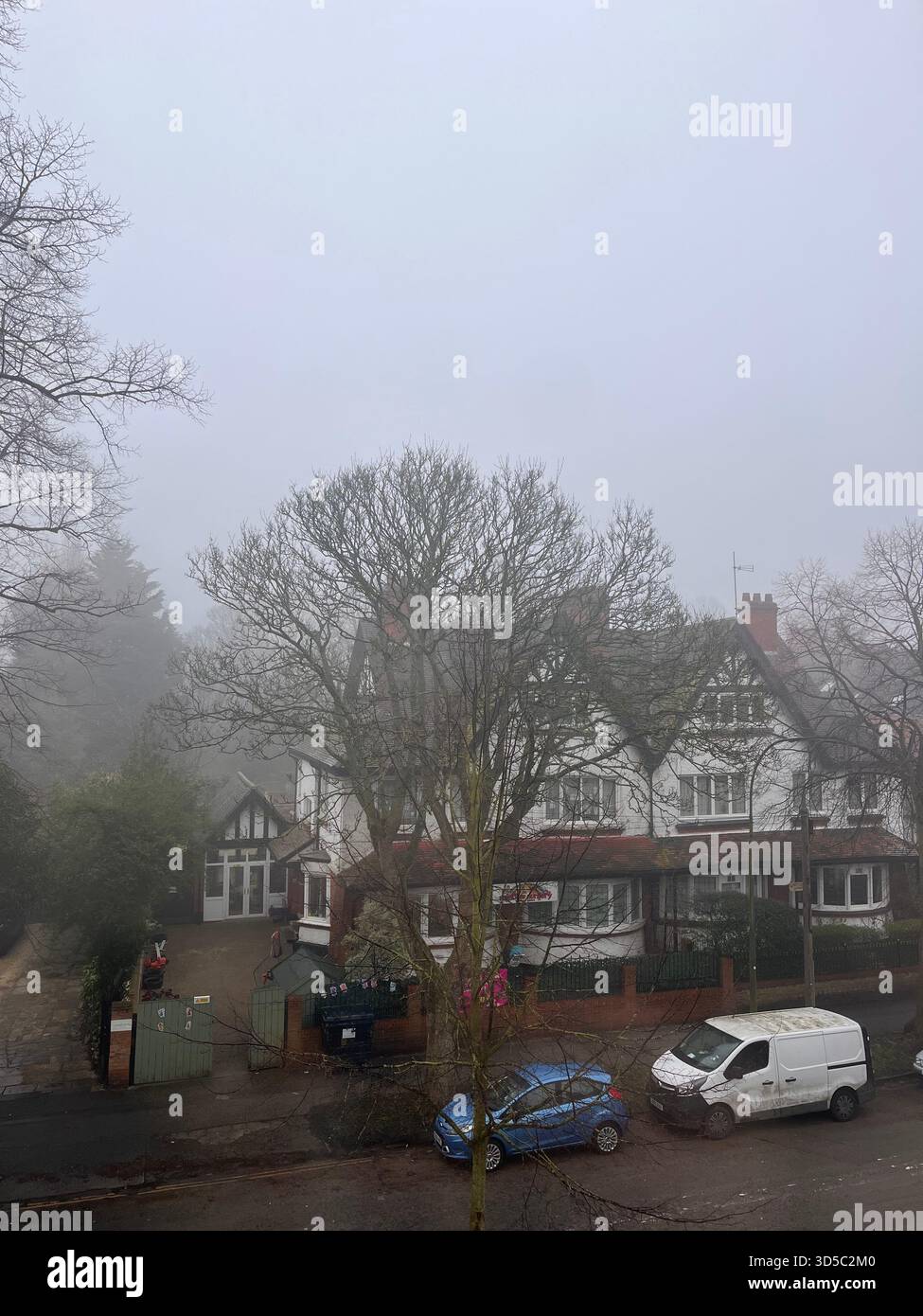 Nebelige Morgenszene mit traditionellen Backsteinhäusern und geparkten Autos in einer ruhigen Wohnstraße im dichten Nebel in Hull, England. - Smartphone-aufgenommenes Stockfoto