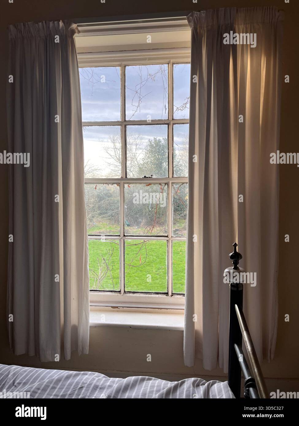 Heller Morgenblick durch ein klassisches Schiebefenster mit Vorhängen, Blick auf ein grünes Feld in Hull, England, schafft eine friedliche und gemütliche Landschaft - Smartphone-aufgenommenes Stockfoto