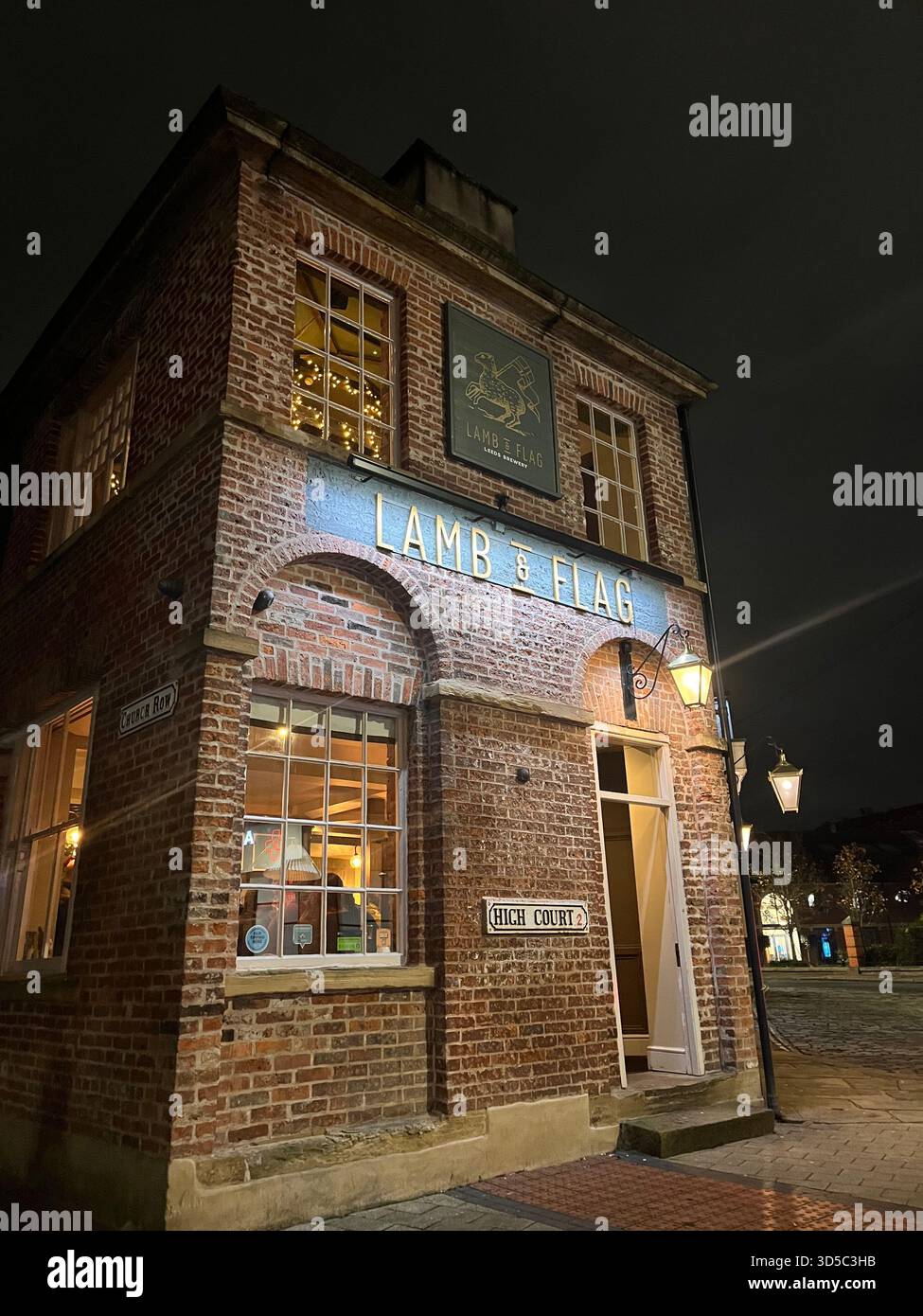 Nachtansicht auf ein traditionelles gemauertes Wirtshaus mit beleuchteten Fenstern und Schildern in Leeds, England. Historische britische Architektur und warme Straße Stockfoto