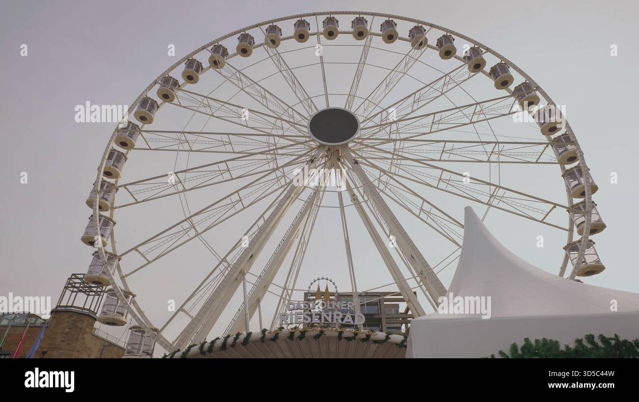 Ein großes Riesenrad ragt über einem Festivalgelände und schafft eine lebhafte Atmosphäre in der urbanen Landschaft. Stockfoto