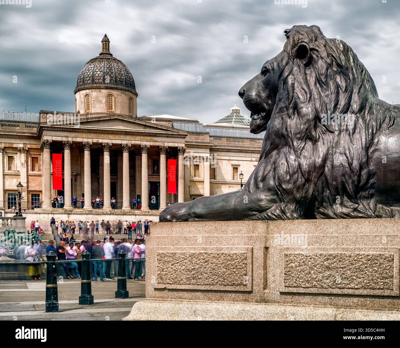 London, Großbritannien - 14. Mai 2018: Löwenstatue am Trafalgar Square mit der National Gallery im Hintergrund an einem bewölkten Tag im Zentrum Londons. Stockfoto