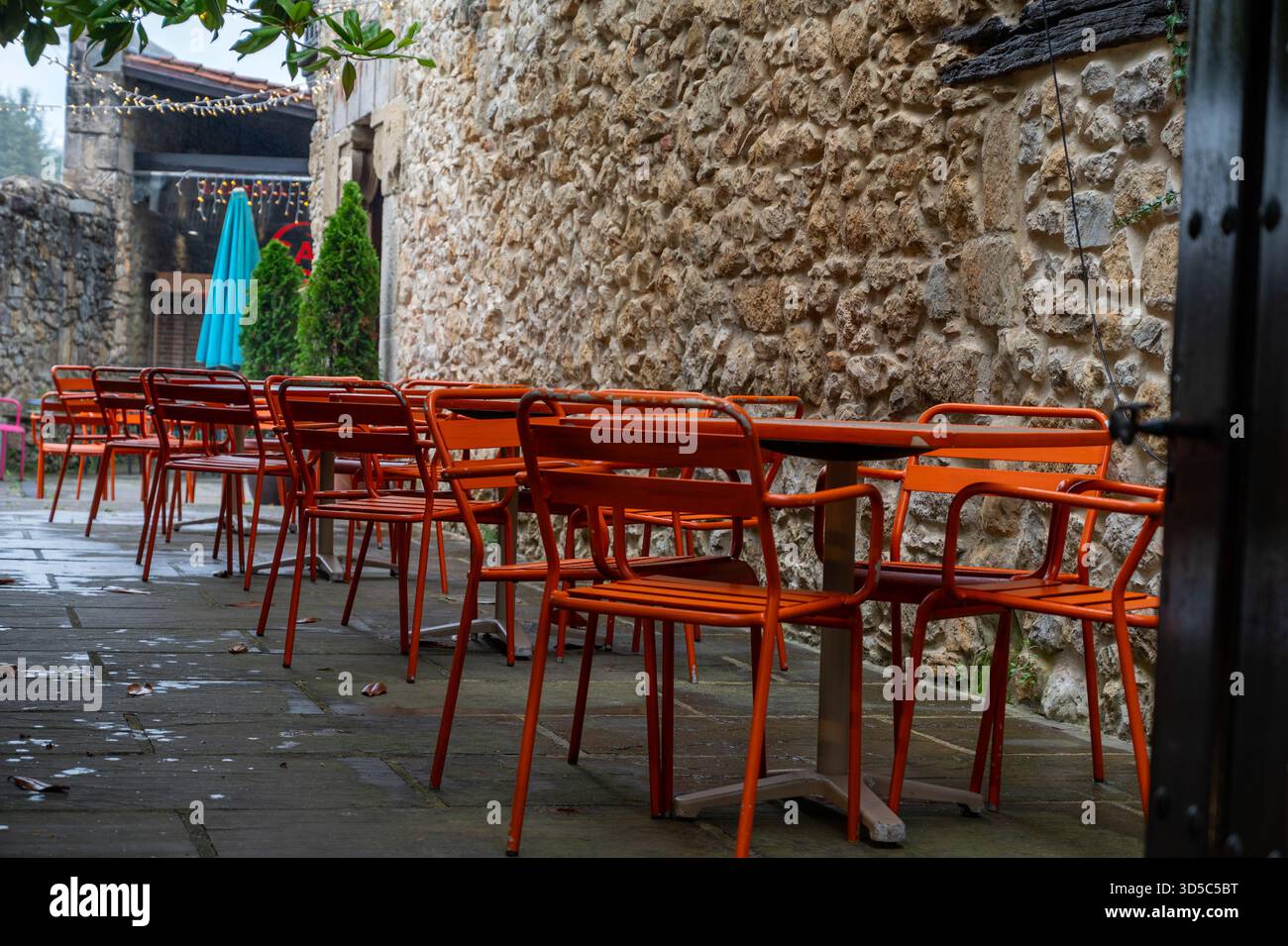 Eine Reihe oranger Stühle und Tische sitzen draußen im Regen. Die Stühle sind in einer Reihe angeordnet, einige zur Wand und andere zur Straße Stockfoto