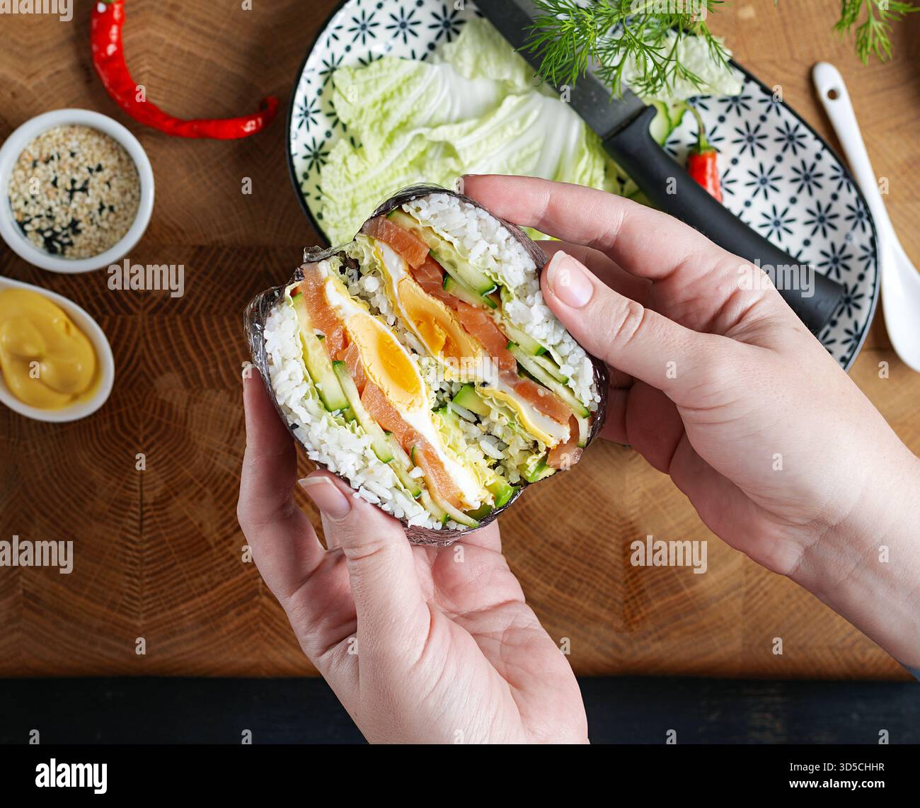 Ein kreativer Sushi-Burger mit Lachs, Spiegelei, Käse, Gurke und Avocado in den Händen einer Frau. Stockfoto