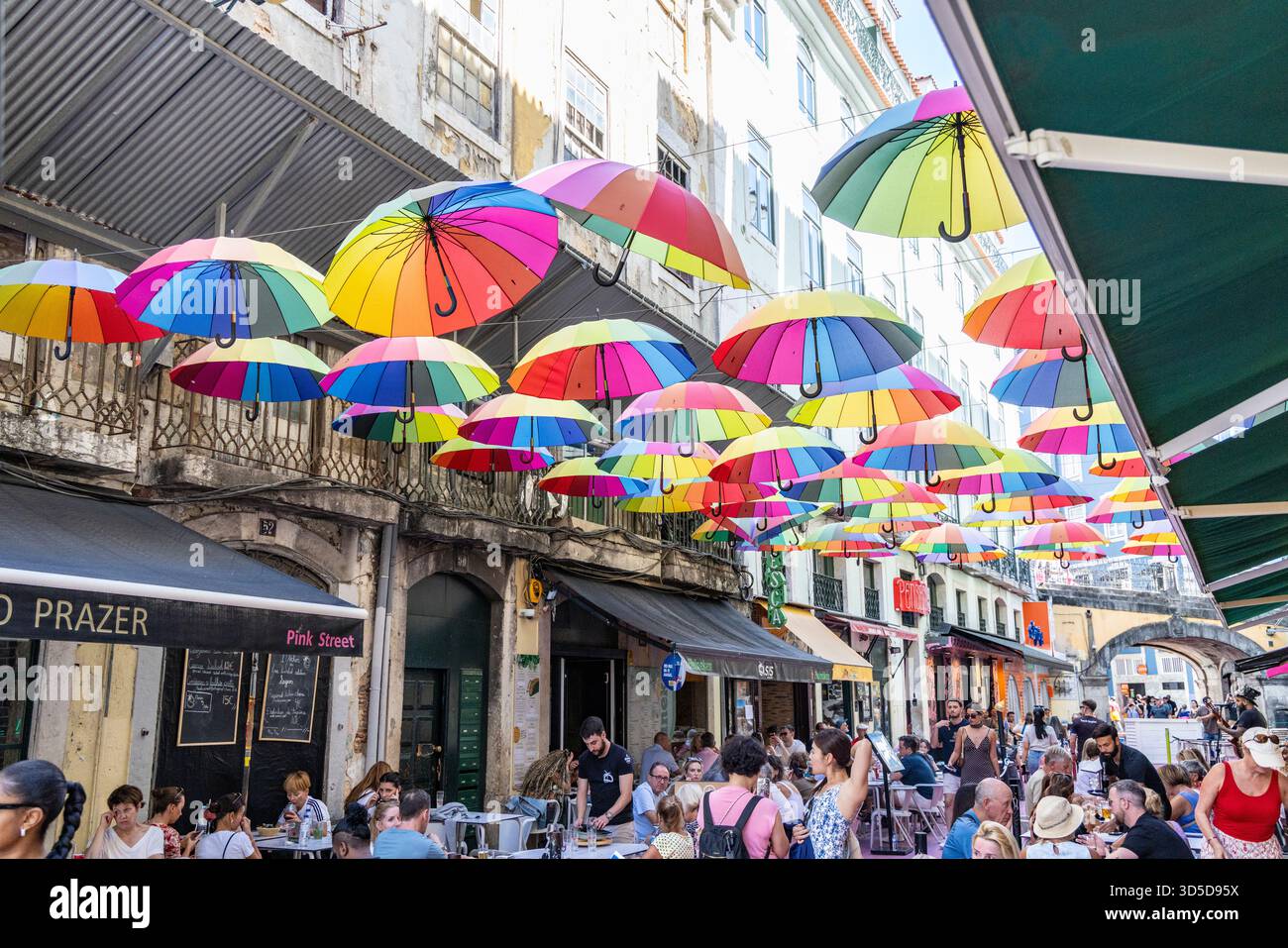 Rosa Straße Lissabon, offiziell Rua Nova do Carvalho genannt, Straße mit rosa Pflaster und mehrfarbigen Regenschirmen, die darüber hängen, Portugal, Europa Stockfoto