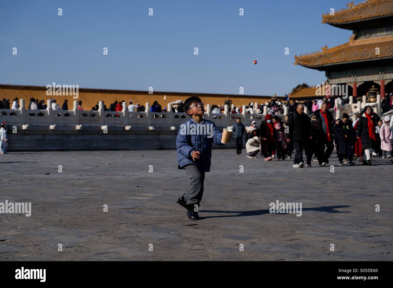 Junge in blauer Jacke jagt einen fliegenden Ball mit einem Papierbecher in einem der Höfe der Verbotenen Stadt Stockfoto