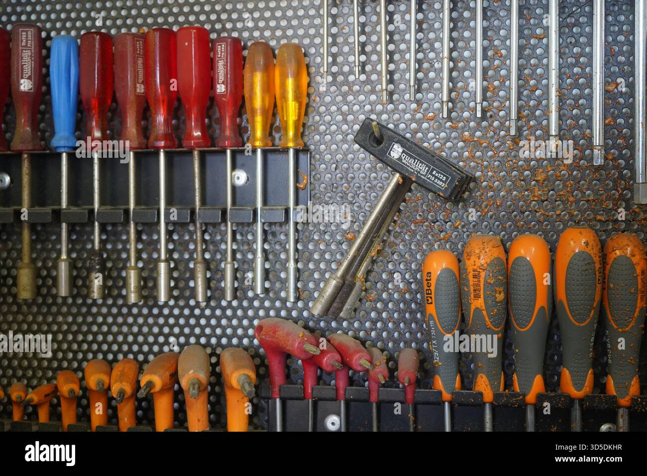 Eine dynamische Aufnahme verschiedener Handwerkzeuge, einschließlich Schraubendreher, Innensechskantschlüssel und einem T-Griff-Schraubenschlüssel, bedeckt mit Sägemehl auf einer Werkstattpinnwand. Stockfoto