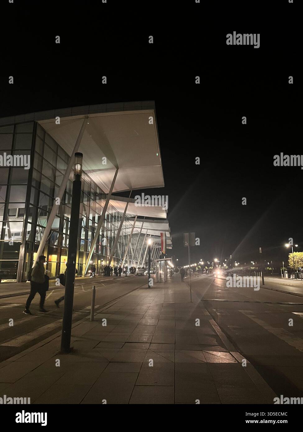 Ein nächtlicher Blick auf das Terminal des Flughafens Wrocław in Polen mit moderner Glasarchitektur und beleuchtetem Fußweg - Smartphone-aufgenommenes Stockfoto