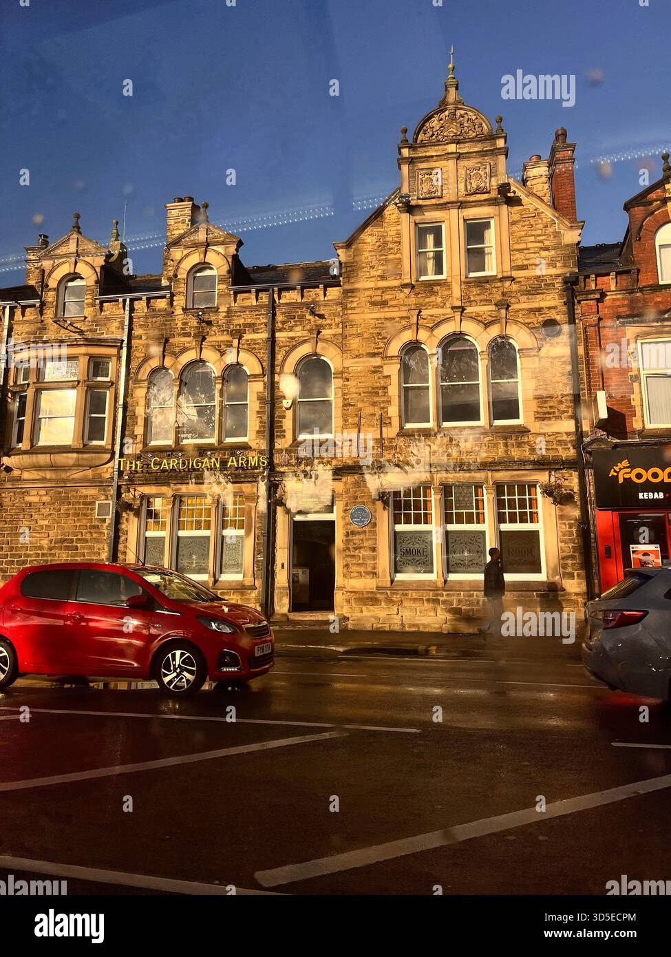 Ein wunderschön beleuchtetes historisches Steingebäude in Leeds, England, fotografiert bei Nacht mit warmer Beleuchtung und einem Auto, das im Vordergrund vorbeifährt. Stockfoto