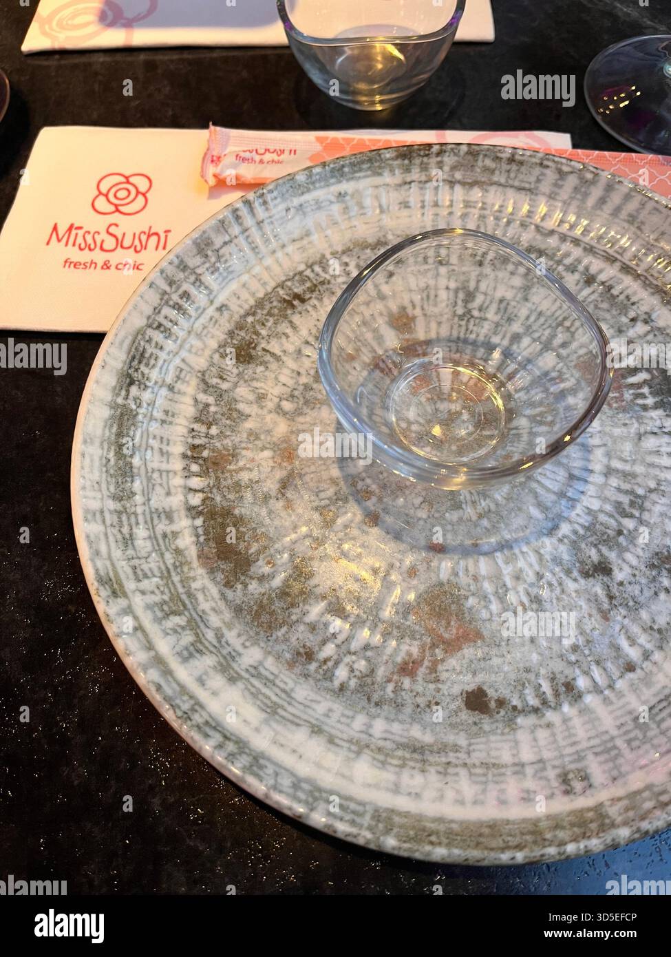 Nahaufnahme einer strukturierten Glasplatte mit einer leeren Tasse auf einem Restauranttisch in Alicante, Spanien. - Smartphone-aufgenommenes Stockfoto